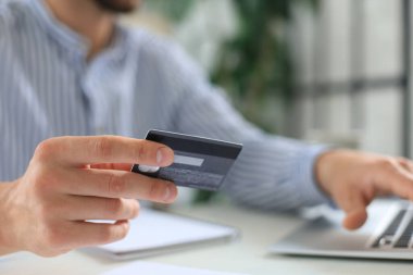Genç adam ofisinde oturuyor ve kredi kartıyla tabletiyle ödüyor.