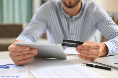 Genç adam ofisinde oturuyor ve kredi kartıyla tabletiyle ödüyor.