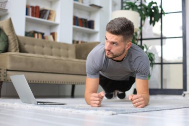 Karantina sırasında evde tahta egzersizi yapan çekici bir adam. Fitness sağlığın anahtarıdır