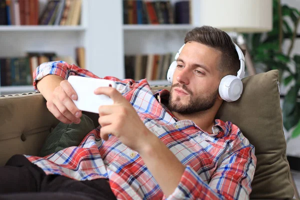 Attractive Young Man Relaxing Couch Home Listening Music Playing Smartphone — Stock Photo, Image