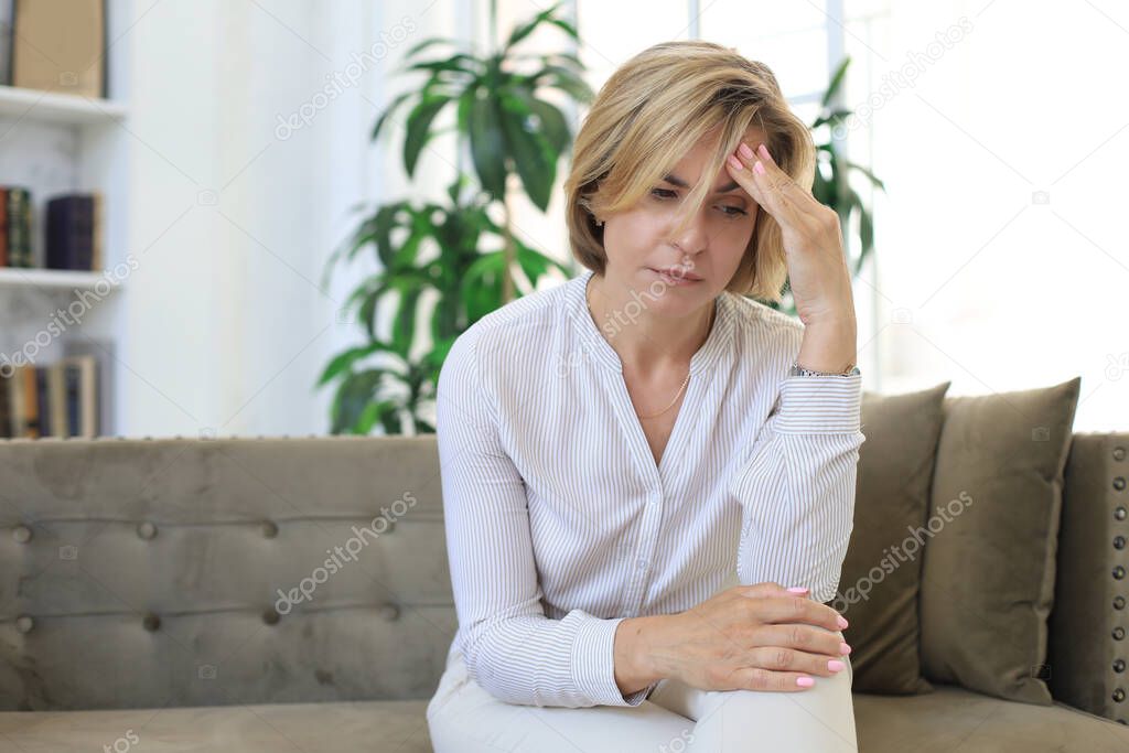 Unhappy middle aged woman sitting on a sofa in the living room