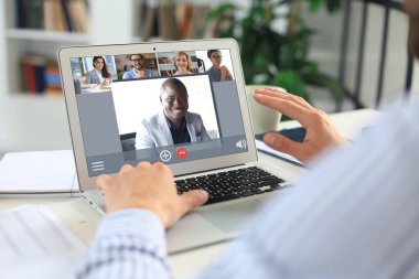 Kulaklıklı bir iş adamı video konferansında iş arkadaşlarıyla konuşuyor. Şirketlerinin mali raporlarını tartışmak için evde dizüstü bilgisayarla çalışan çok ırklı iş adamları..