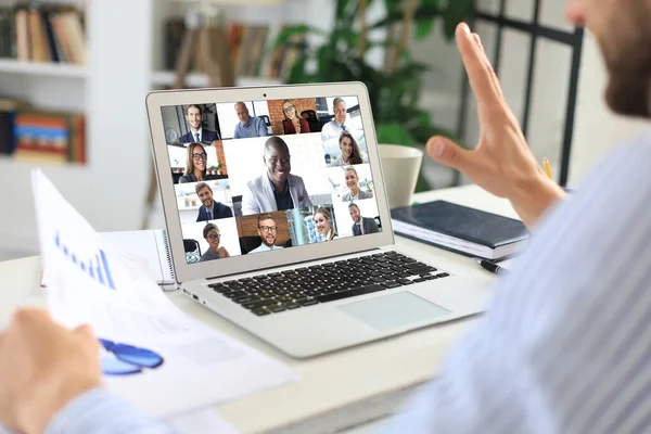 Uomo d'affari in cuffia che parla con i suoi colleghi in videoconferenza. Team aziendale multietnico che lavora da casa utilizzando il computer portatile, discutendo il rapporto finanziario della loro azienda. — Foto Stock