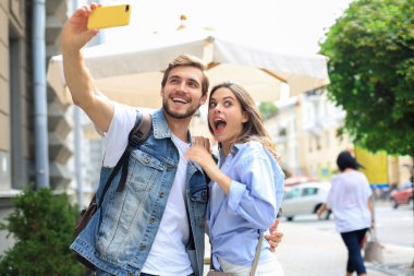 Güzel, genç bir çift şehrin sokaklarında yürüyor, selfie çekerken sarılıyorlar.