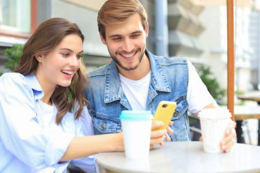 Çekici, genç bir çift kahve içerken açık kafede oturuyor, cep telefonu kullanıyor.