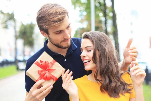 Image of charming excited couple in summer clothes smiling and holding present box outdoor