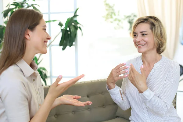 Happy middle aged mother and daughter talking on sofa in living room