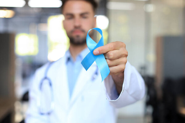 Doctor hand with blue prostate cancer awareness ribbon. Medicine oncology closeup sky symbol