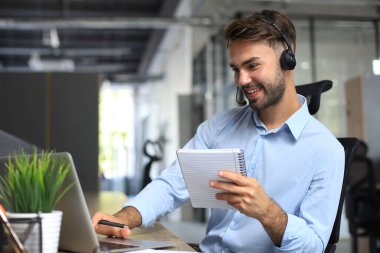 Modern ofiste oturan, kulaklıklı, gülümseyen bir iş danışmanı, bilgisayar ekranına bakan bir video. Müşteri hizmetleri destek hattı çevrimiçi sohbet ediyor.