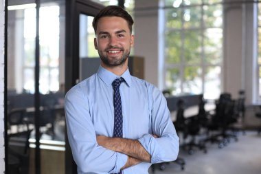 Genç yakışıklı işadamı ofis ortamında gülümsüyor.