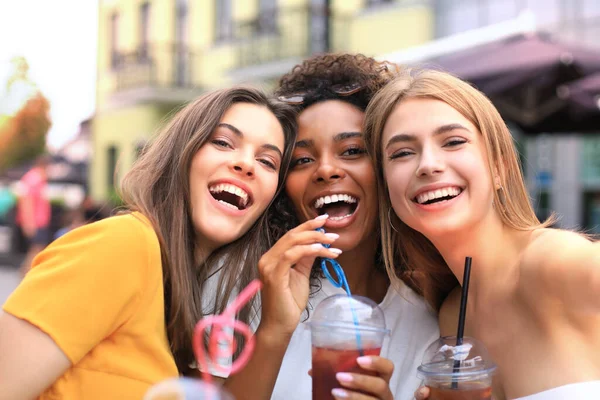 Três meninas hipster cool na moda, amigos bebem coquetel no fundo da cidade urbana. — Fotografia de Stock