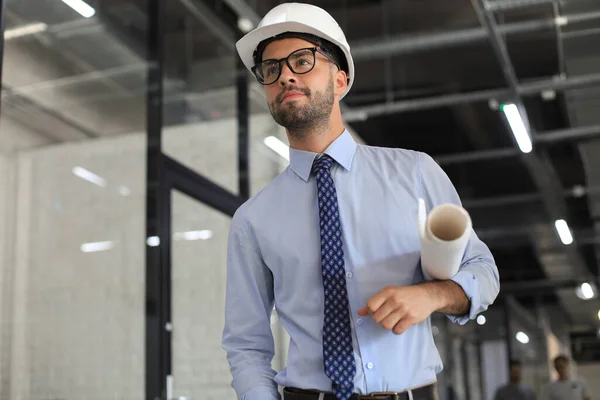 Joven Hombre Negocios Confiado Hardhat Sosteniendo Plano Mirando Hacia Otro —  Fotos de Stock