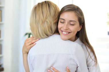 Neşeli genç kadın orta yaşlı annesini oturma odasında kucaklıyor.