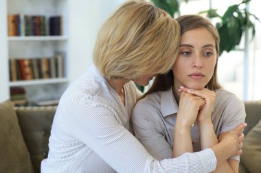 Orta yaşlı anne ve kızı oturma odasında kanepede konuşuyor.