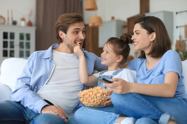 Mutlu ve çocuklu bir aile kanepede oturur televizyon izler ve patlamış mısır yer, genç ebeveynler kızlarını kucaklar birlikte kanepede dinlenirler.