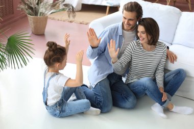 Küçük çocuklu mutlu bir aile, sıcak zeminde oturup birlikte dinlenir, çok mutlu ebeveynler dinlenir. Hafta sonunun tadını çıkarın. Küçük kızınızla eğlenin, beşlik çakın.