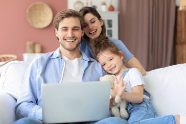 Küçük kızıyla birlikte kanepede oturan, laptoptaki video görüşmelerine cevap veren ve hafta sonları evde dinlenirken el sallayan olumlu, arkadaş canlısı ebeveynler.