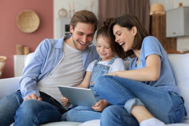 Gülümseyen küçük kızıyla olumlu arkadaş canlısı ebeveynler hafta sonu evde dinlenirken dijital tabletteki video çağrılarına cevap veriyorlar.