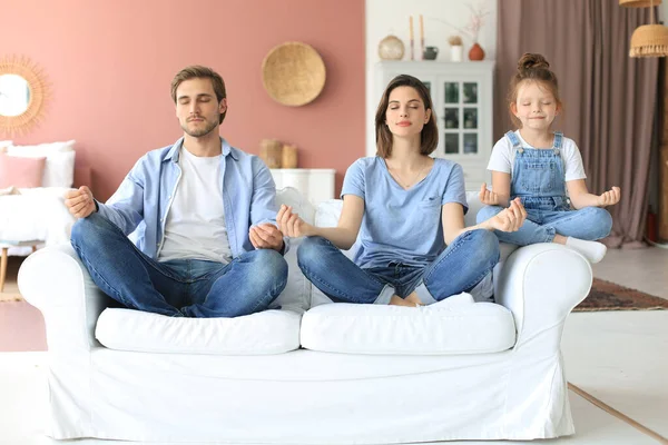 Küçük kızıyla sakin genç bir aile, birlikte kanepede yoga yapar, küçük bir anaokulu çocuğuyla mutlu ebeveynler, kanepeye dinlenir, hafta sonları evde negatif duygulardan arınırlar.