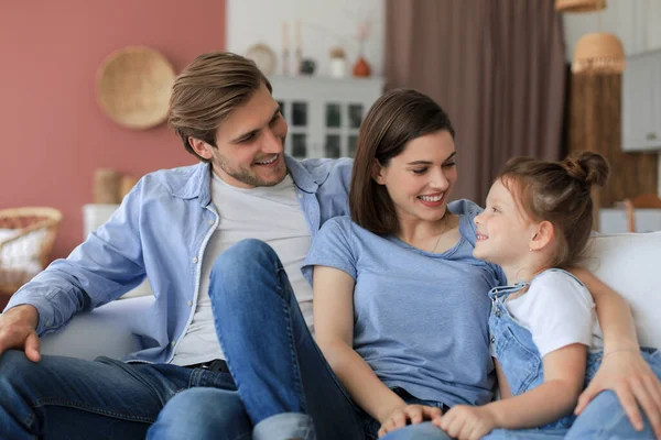 积极友善的年轻父母 他们的小女儿笑着坐在沙发上 周末在家里放松一下 — 图库照片