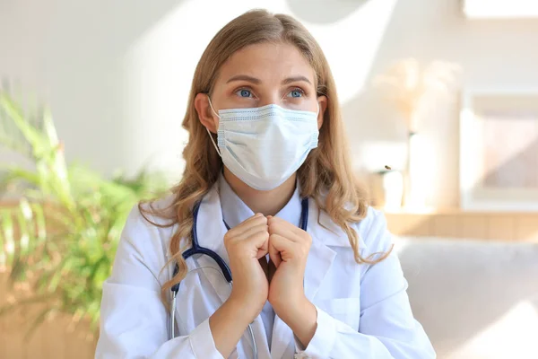 Woman doctor in a mask praying while sitting in medical office
