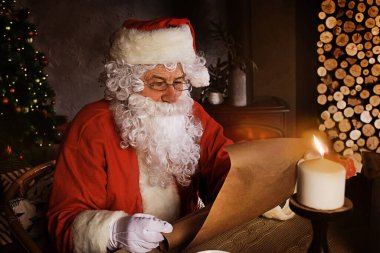 Mutlu Noel Baba 'nın portresi Noel ağacının yanındaki odasında oturuyor ve Noel mektubu ya da dilek listesi okuyor.