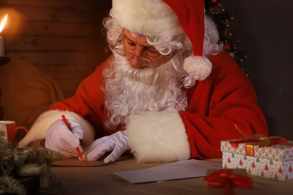圣诞老人坐在他家靠近圣诞树的房间里 回复圣诞信的画像 — 图库照片