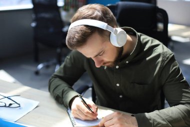 Düşünceli genç iş adamı modern ofiste çalışırken bir şeyler yazıyor.