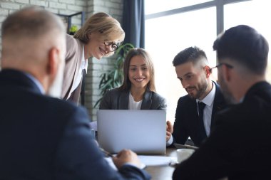 Girişim ekibi, modern parlak ofis içinde toplantı ve dizüstü bilgisayar üzerine çalışıyor