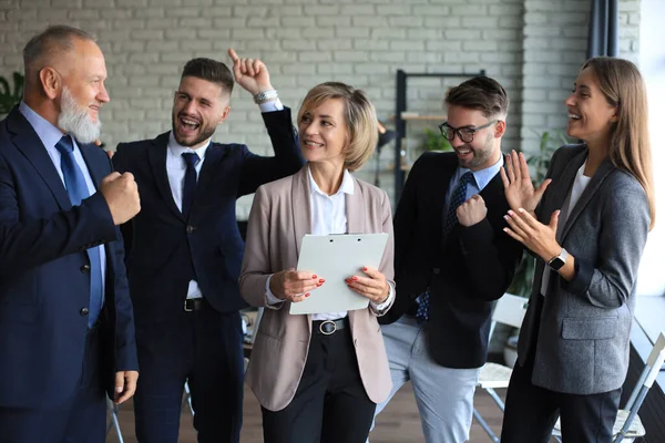 Heureux hommes d'affaires modernes gardent les bras levés et expriment joyeuse tandis que debout dans le bureau. — Photo