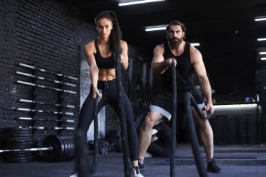 Savaş halatıyla atletik genç çift spor salonunda egzersiz yapıyor.