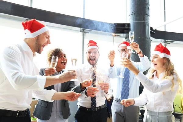 Young business partners are lighting bengal lights and drinking champagne in a modern office. Merry Christmas and Happy New Year