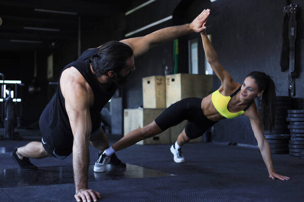 Sporty couple doing push ups and giving high five to each other in gym