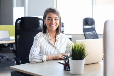 Genç ve güzel iş kadını modern ofiste defter bilgisayarında çalışıyor.