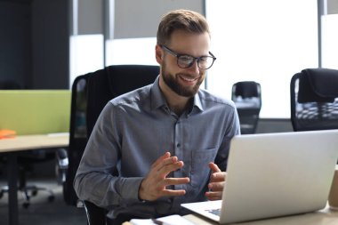 Gülümseyen genç iş adamı ofiste video görüşmesi yapıyor.