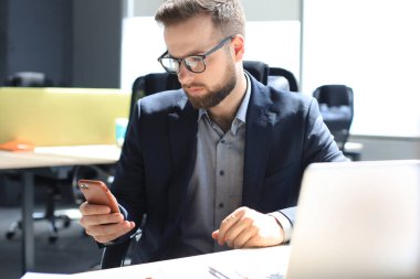 İş adamı ofisteki cep telefonunu kullanıyor.