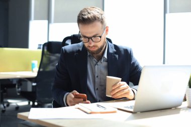 İş adamı ofisteki cep telefonunu kullanıyor.