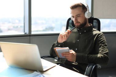 Genç, modern iş adamı ofiste otururken dizüstü bilgisayar kullanıyor.