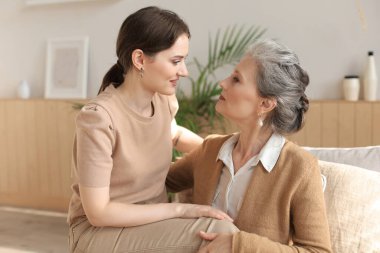 Yaşlı, orta yaşlı anne sevinçle koltukta oturuyor ve kızını dizlerinin üstüne çöktürüyor. Mutlu ve güvenilir ilişkiler. Aile kavramı