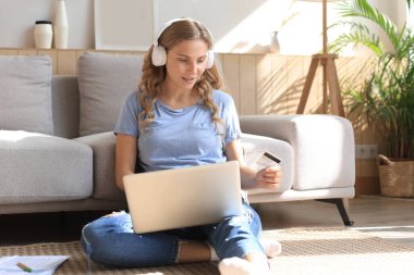 Oturma odasında kredi kartı ve laptop kullanan mutlu doğal sarışın.