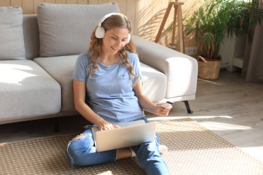 Oturma odasında kredi kartı ve laptop kullanan mutlu doğal sarışın.