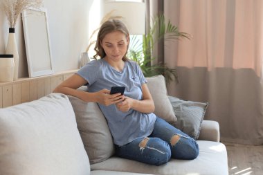 Güzel kız evdeki kanepede akıllı telefonunu kullanıyor.