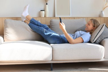 Güzel kız evdeki kanepede akıllı telefonunu kullanıyor.