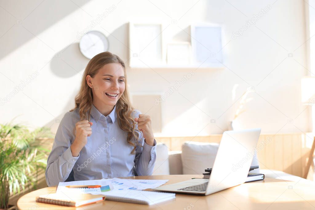 Happy entrepreneur woman sit at desk reading good news and express joy rising hands up