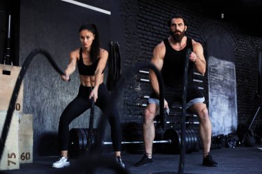 Savaş halatıyla atletik genç çift spor salonunda egzersiz yapıyor.