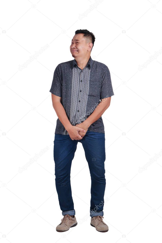 Photo image of funny Asian man crying close his eyes, gesturing as if he is having pain in his sensitive area want to pee urinating