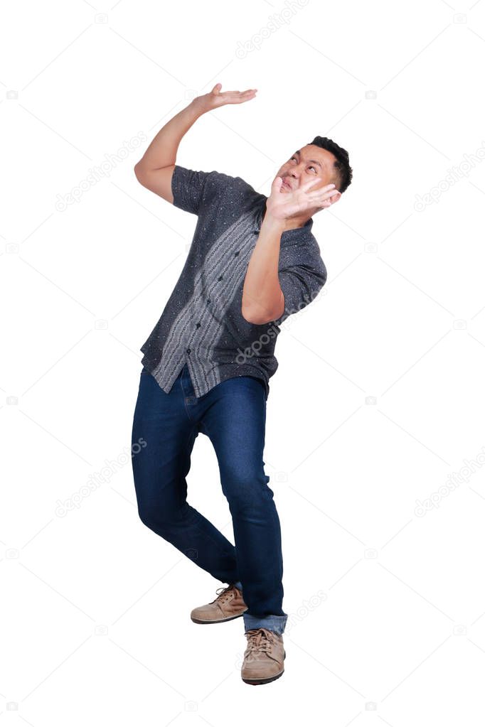 Asian man wearing batik shirt protects hands from what is falling from above. Man holding a heavy load. Isolated over white background