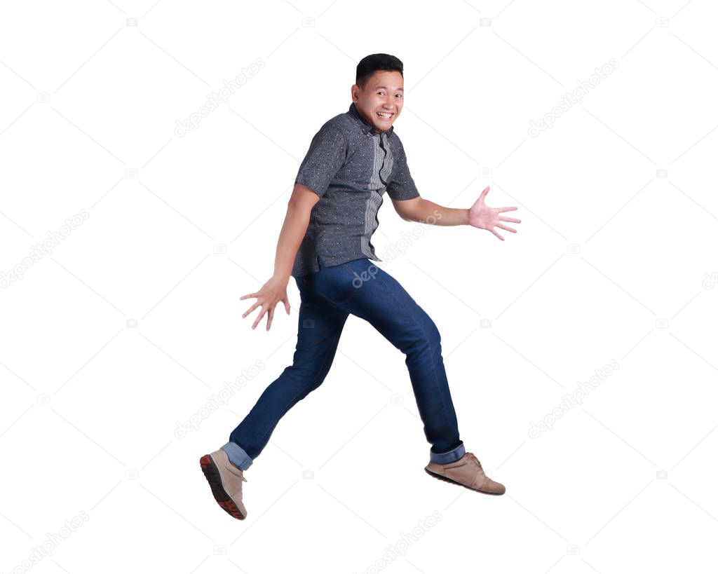 Happy young Asian man walking on air, wearing blue jeans and batik shirt. Isolated on white. Full body portrait.