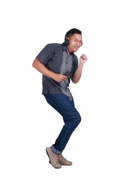 Mavi jeans ve müzik ve mutlu bir şekilde dans batik forması giyen genç Asyalı adam. Beyaz izole. Tam vücut portre