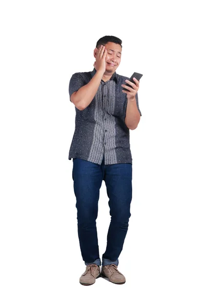 年轻的亚裔男子身穿蓝色牛仔裤和蜡染衫的电话哭着 坏消息的表情 被隔离在白色 全身肖像 — 图库照片